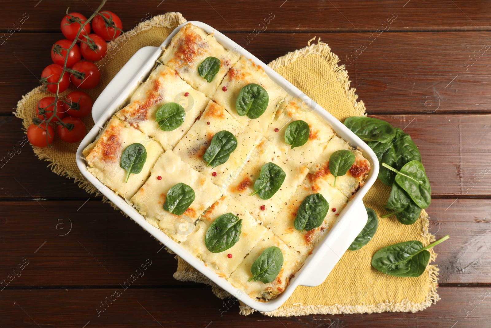 Photo of Delicious spinach lasagne in baking dish and fresh tomatoes on wooden table, flat lay