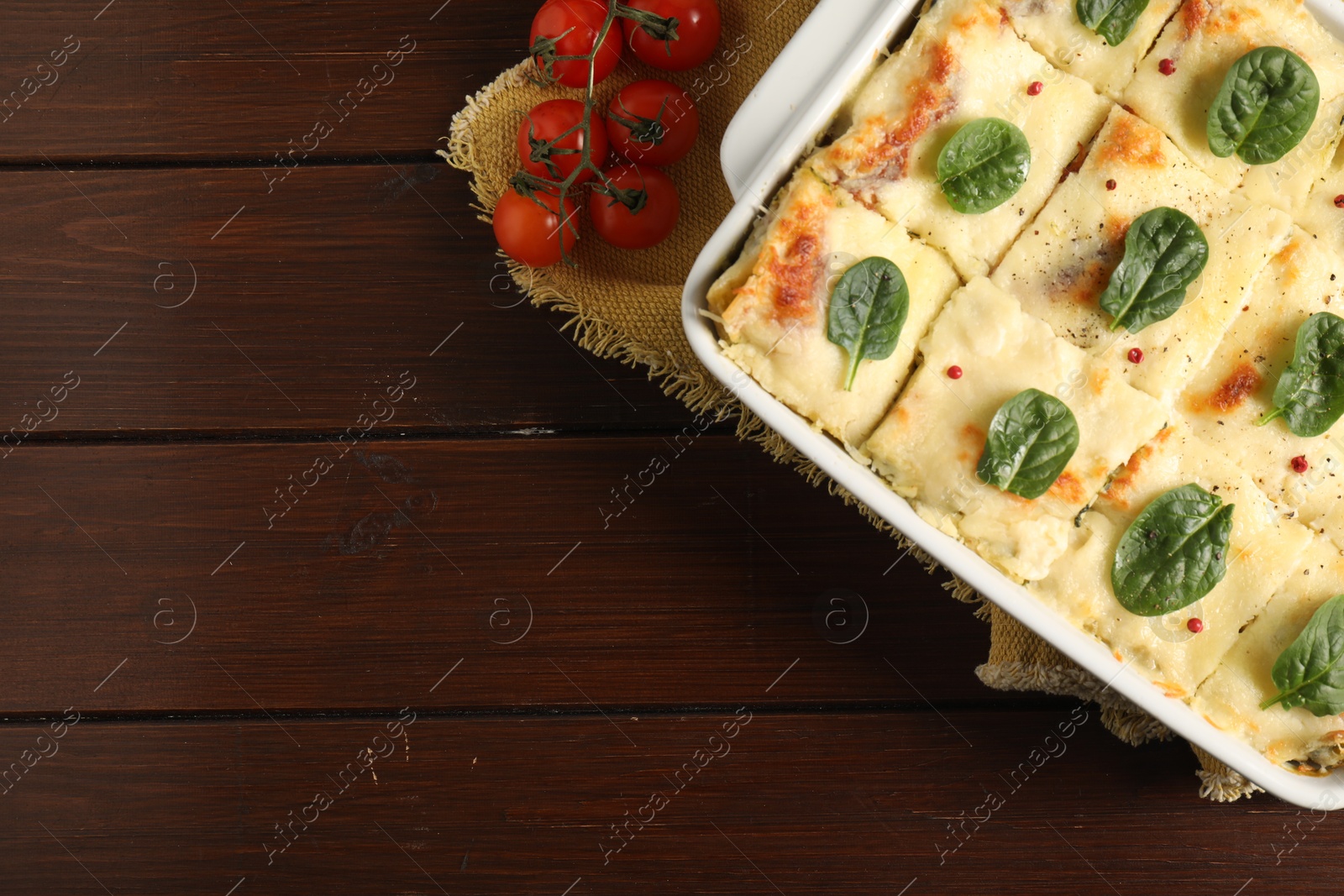 Photo of Delicious spinach lasagne in baking dish and fresh tomatoes on wooden table, flat lay. Space for text