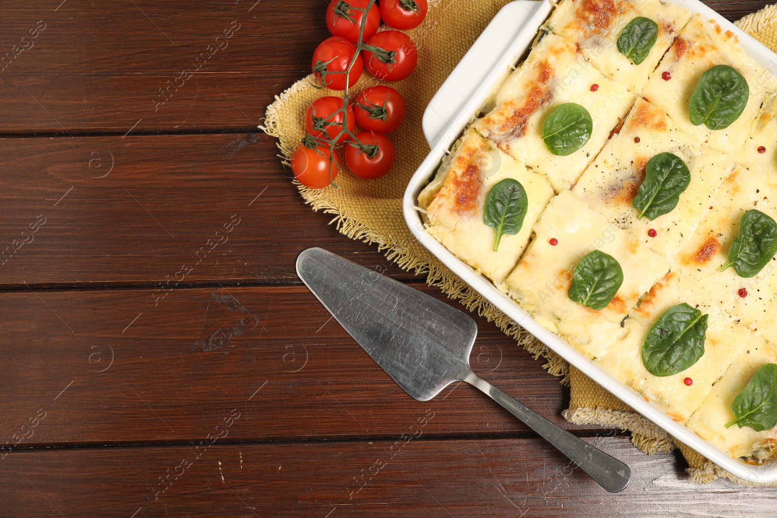 Photo of Delicious spinach lasagne in baking dish served on wooden table, flat lay. Space for text