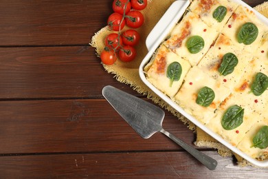 Photo of Delicious spinach lasagne in baking dish served on wooden table, flat lay. Space for text