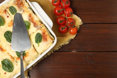 Photo of Delicious spinach lasagne in baking dish served on wooden table, flat lay. Space for text