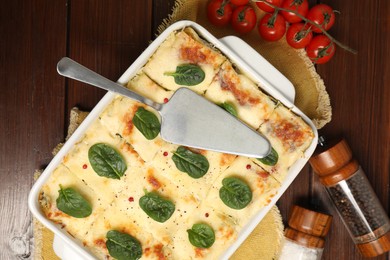 Photo of Delicious spinach lasagne in baking dish served on wooden table, flat lay