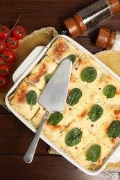 Photo of Delicious spinach lasagne in baking dish served on wooden table, flat lay