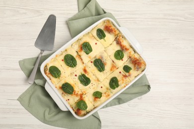 Photo of Delicious spinach lasagne in baking dish served on white wooden table, flat lay