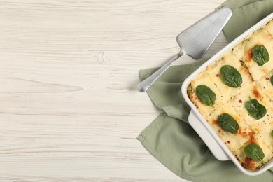 Photo of Delicious spinach lasagne in baking dish served on white wooden table, flat lay. Space for text