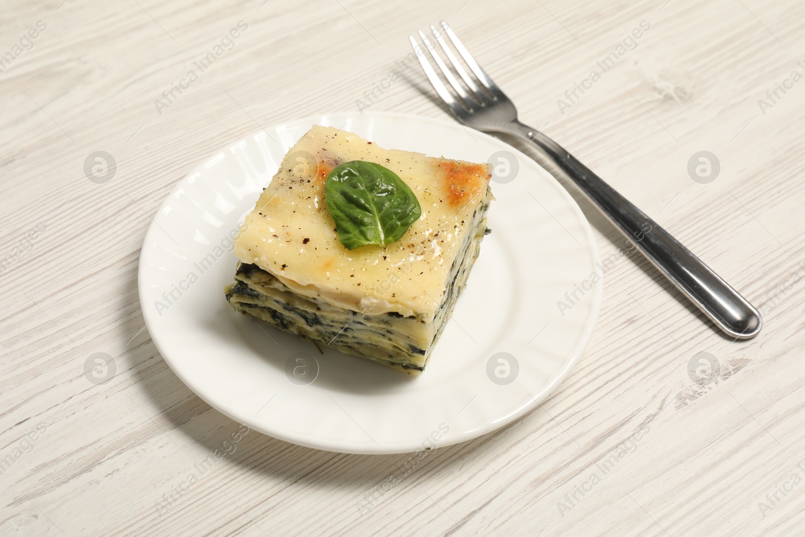 Photo of Piece of delicious spinach lasagne and fork on white wooden table