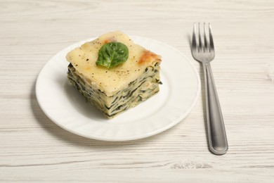 Photo of Piece of delicious spinach lasagne and fork on white wooden table