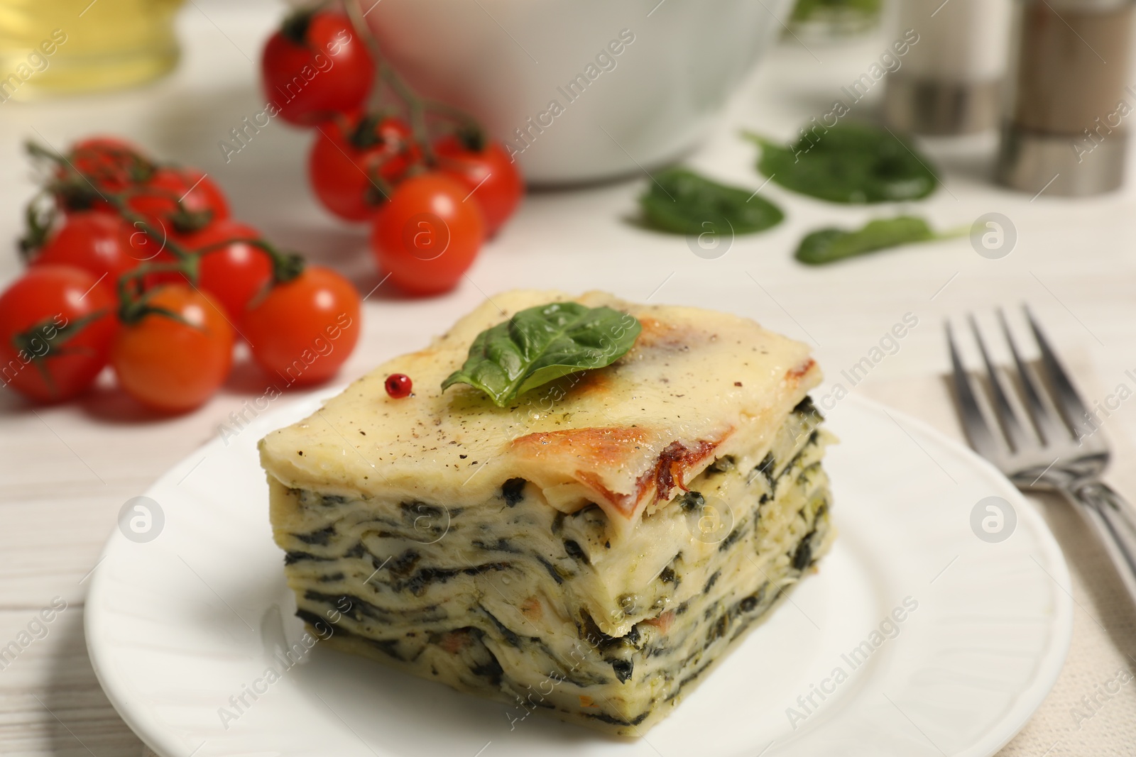 Photo of Piece of delicious spinach lasagne served on white table, closeup