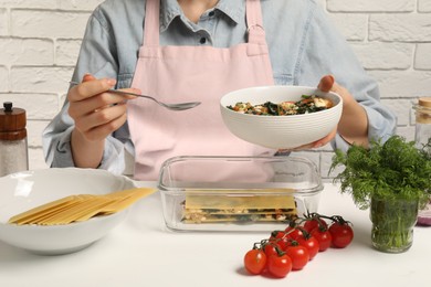 Photo of Woman making spinach lasagna at white table indoors, closeup