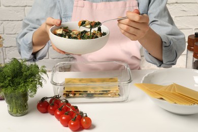 Photo of Woman making spinach lasagna at white table indoors, closeup