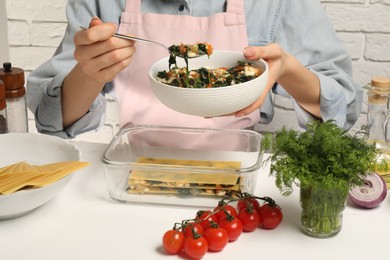 Photo of Woman making spinach lasagna at white table indoors, closeup