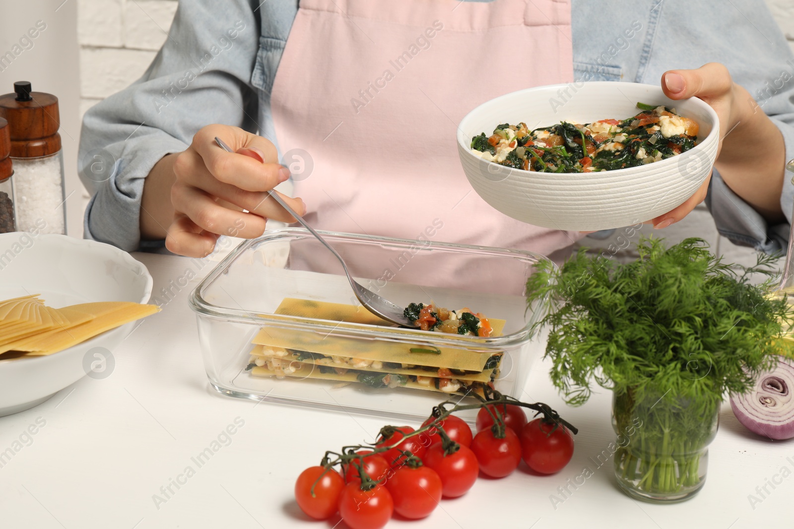 Photo of Woman making spinach lasagna at white table indoors, closeup