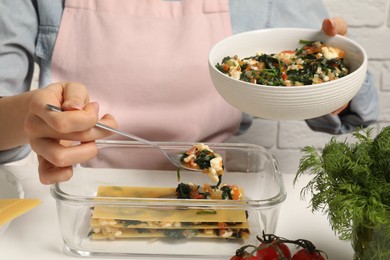 Photo of Woman making spinach lasagna at white table indoors, closeup