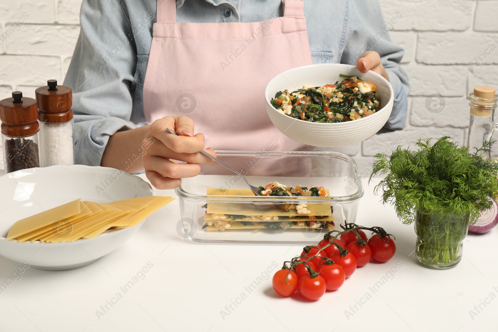 Photo of Woman making spinach lasagna at white table indoors, closeup