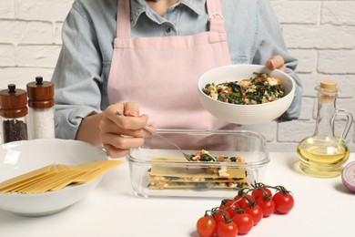 Photo of Woman making spinach lasagna at white table indoors, closeup