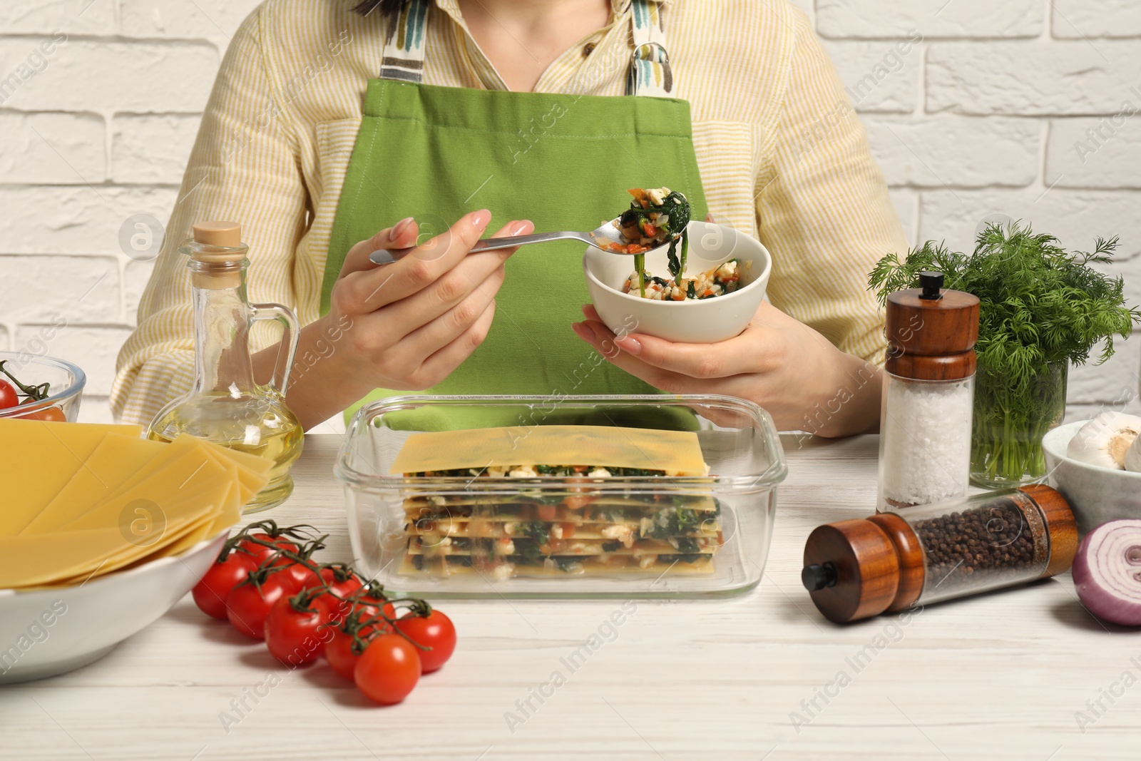 Photo of Woman making spinach lasagna at white wooden table indoors, closeup