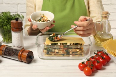 Photo of Woman making spinach lasagna at white wooden table indoors, closeup