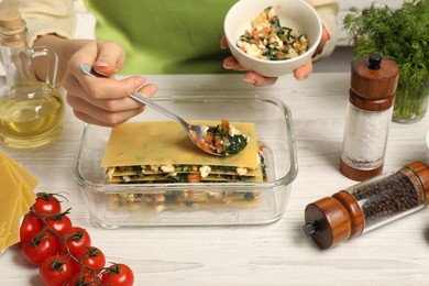 Photo of Woman making spinach lasagna at white wooden table indoors, closeup