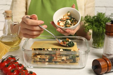 Photo of Woman making spinach lasagna at white wooden table indoors, closeup