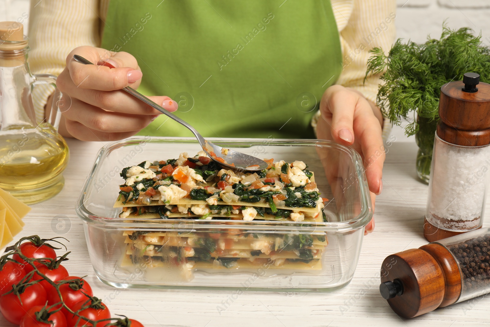 Photo of Woman making spinach lasagna at white wooden table indoors, closeup