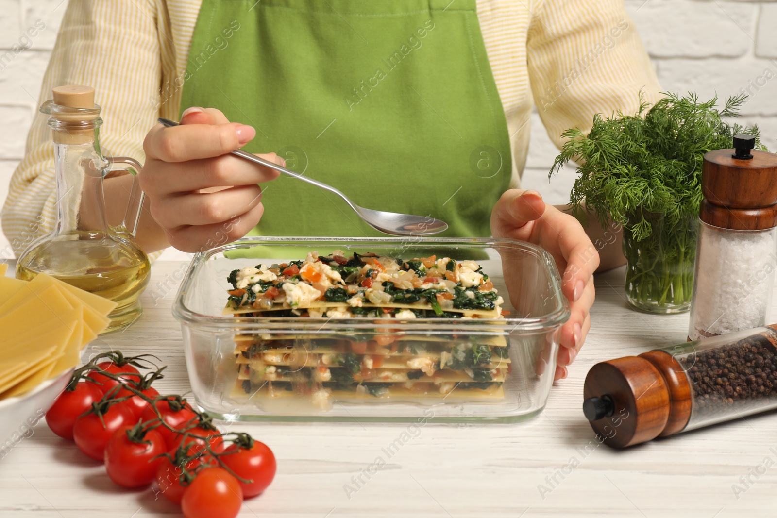 Photo of Woman making spinach lasagna at white wooden table indoors, closeup