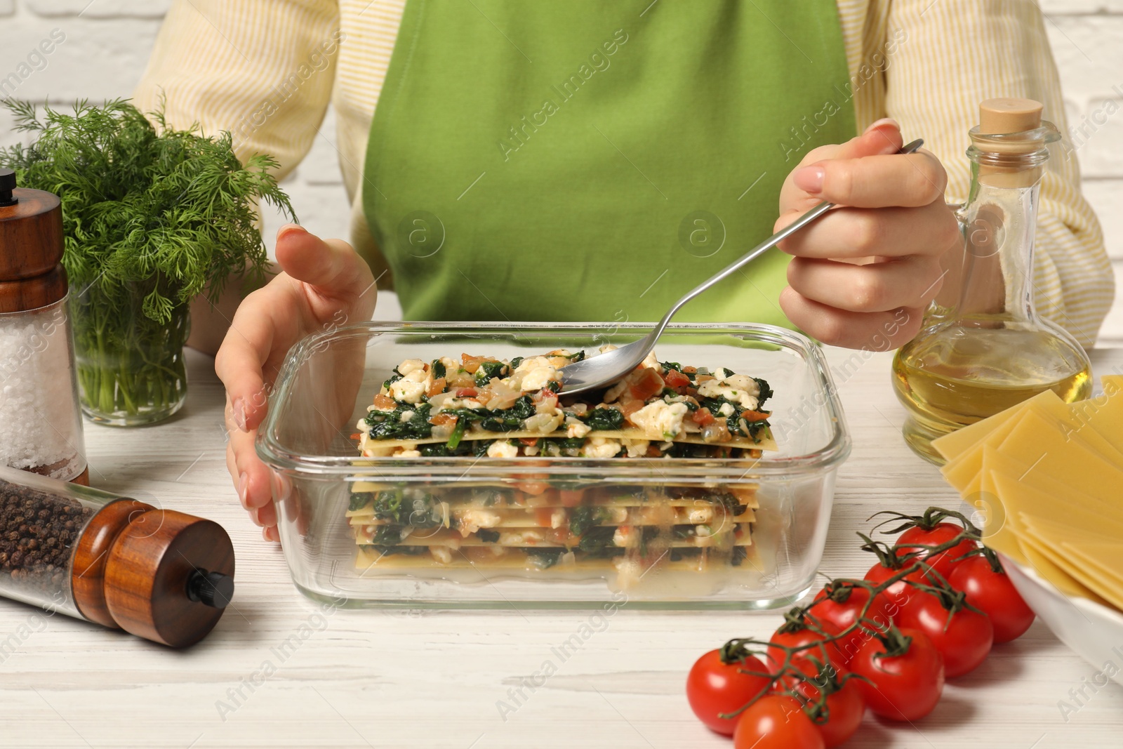 Photo of Woman making spinach lasagna at white wooden table indoors, closeup