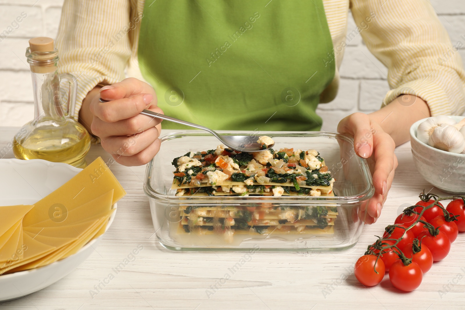 Photo of Woman making spinach lasagna at white wooden table indoors, closeup