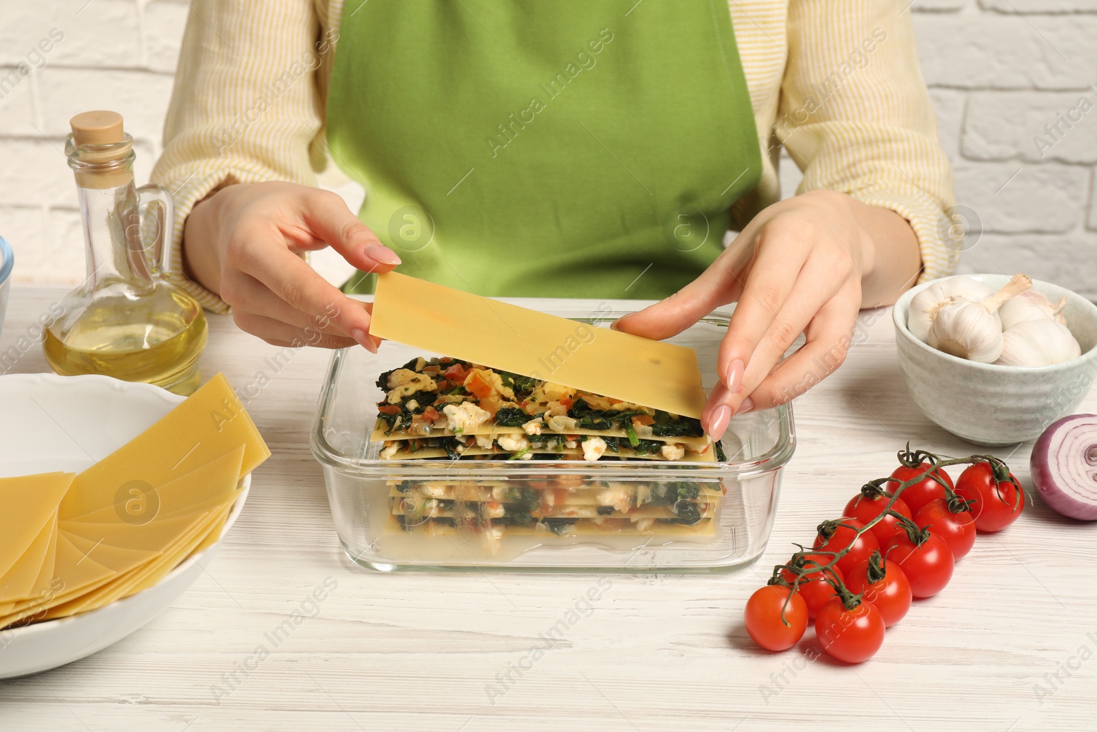 Photo of Woman making spinach lasagna at white wooden table indoors, closeup