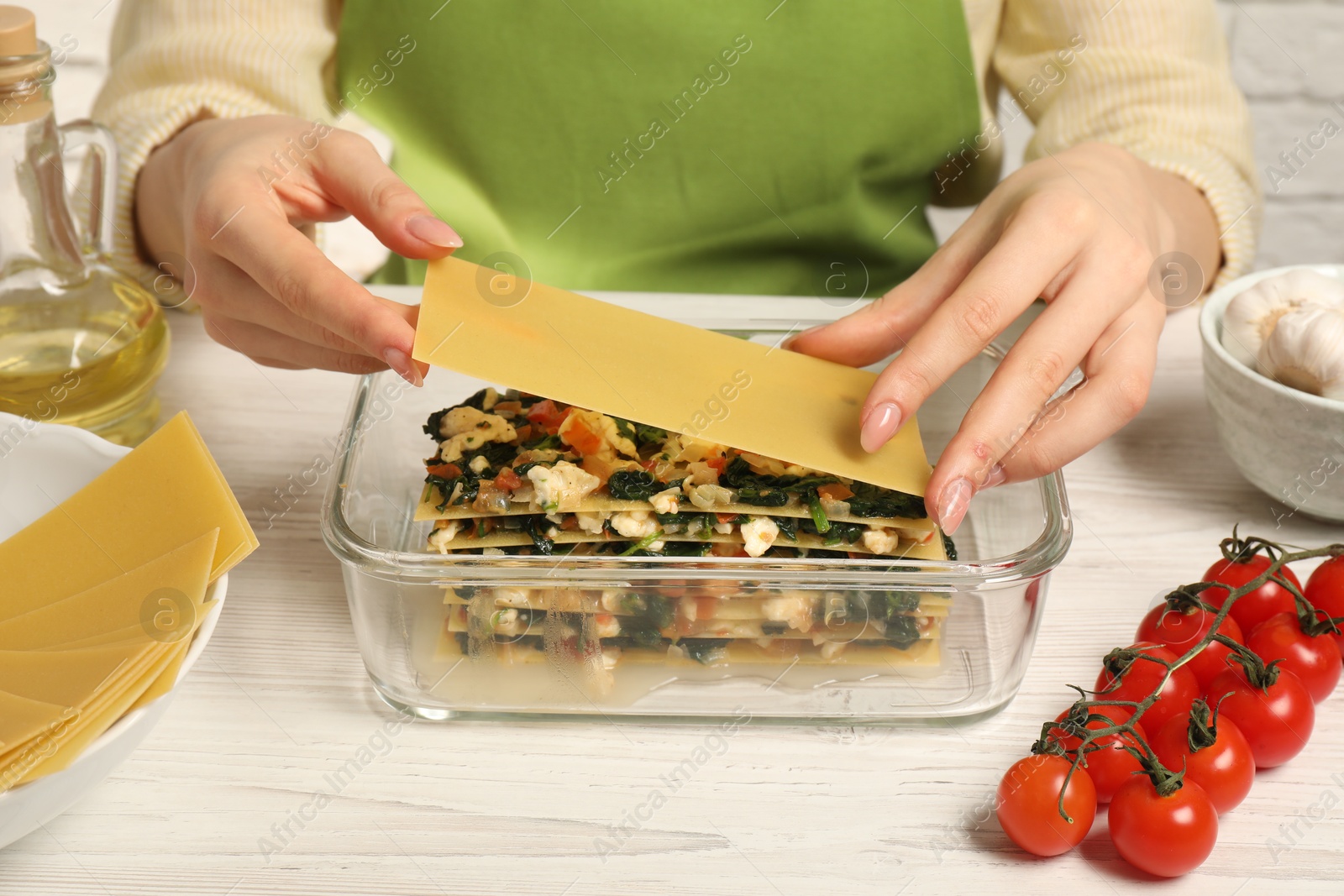 Photo of Woman making spinach lasagna at white wooden table indoors, closeup