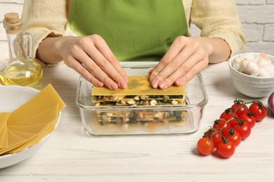 Photo of Woman making spinach lasagna at white wooden table indoors, closeup