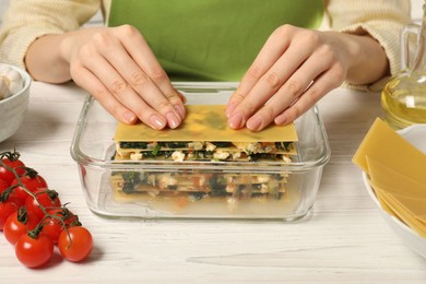 Photo of Woman making spinach lasagna at white wooden table indoors, closeup