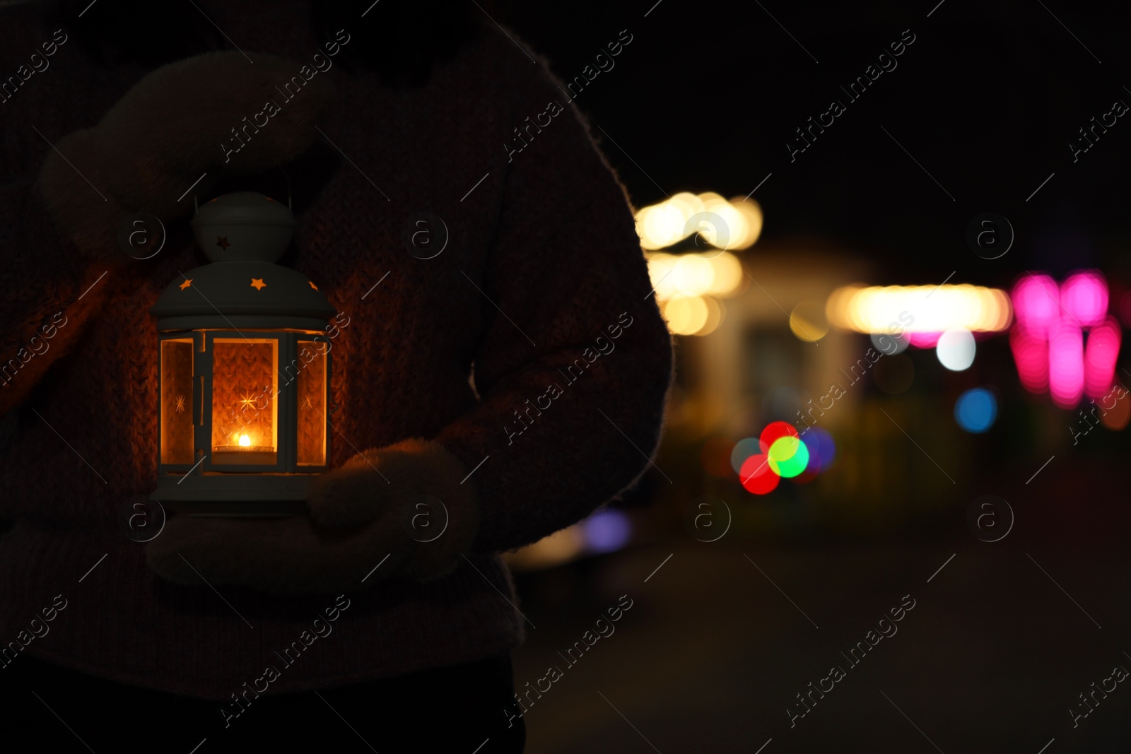 Photo of Woman holding Christmas lantern with burning candle in darkness, closeup and space for text. Bokeh effect