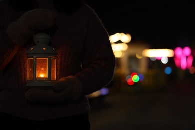 Photo of Woman holding Christmas lantern with burning candle in darkness, closeup and space for text. Bokeh effect