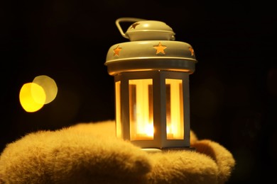 Photo of Woman holding Christmas lantern with burning candle in darkness, closeup