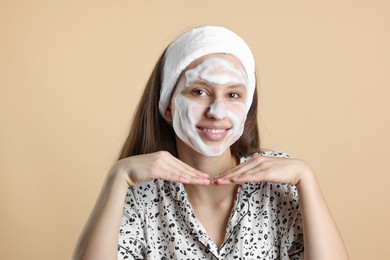 Photo of Teenage girl with cleansing foam on her face against beige background. Acne treatment