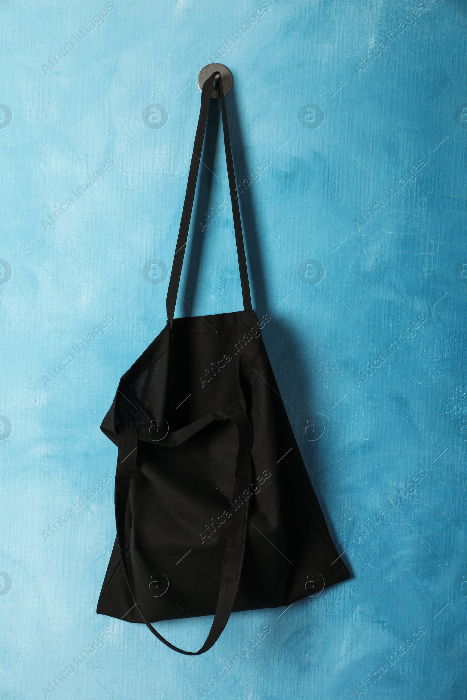 Photo of Black eco bag hanging on light blue wall. Mockup for design