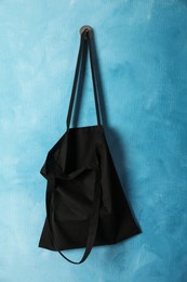 Black eco bag hanging on light blue wall. Mockup for design