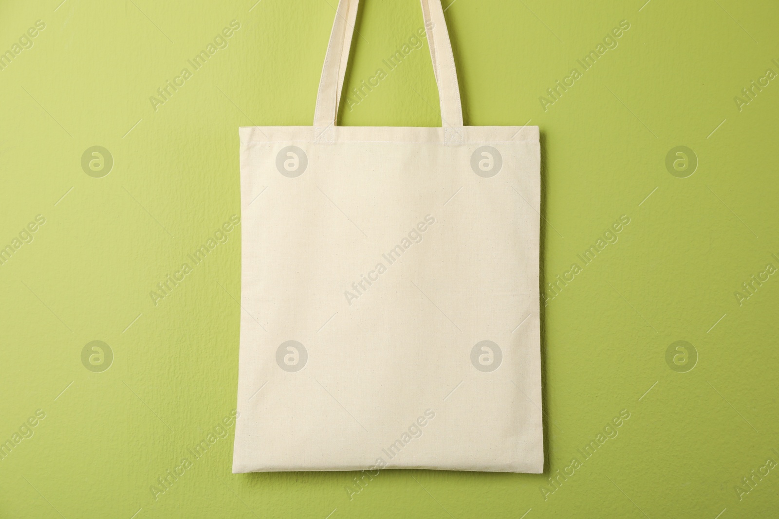 Photo of One eco bag hanging on green wall. Mockup for design