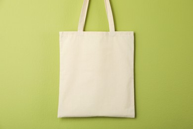 Photo of One eco bag hanging on green wall. Mockup for design