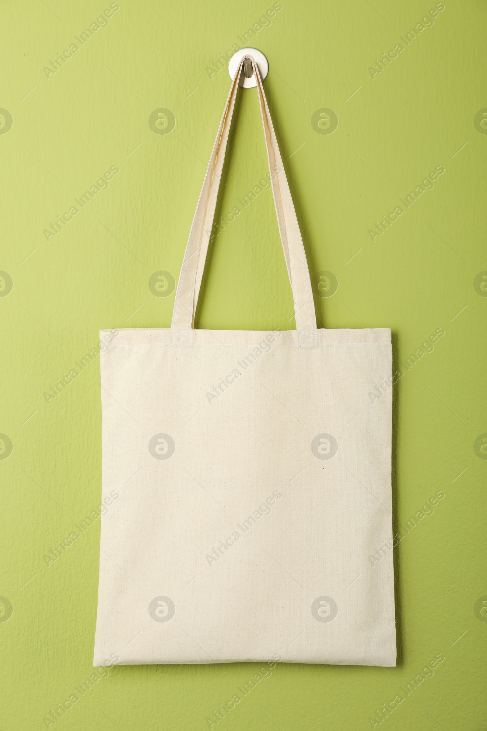 Photo of One eco bag hanging on green wall. Mockup for design