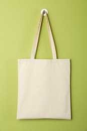 Photo of One eco bag hanging on green wall. Mockup for design