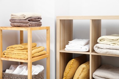 Photo of Home textile organization. Folded towels, blankets and pillows on shelving units indoors, closeup