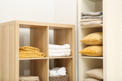 Photo of Home textile organization. Folded towels, blankets and pillows on shelving units indoors, closeup