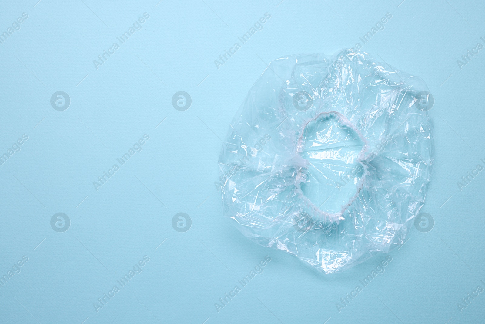 Photo of One shower cap on light blue background, top view. Space for text