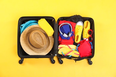 Photo of Travel abroad. Packed suitcase on yellow background, top view