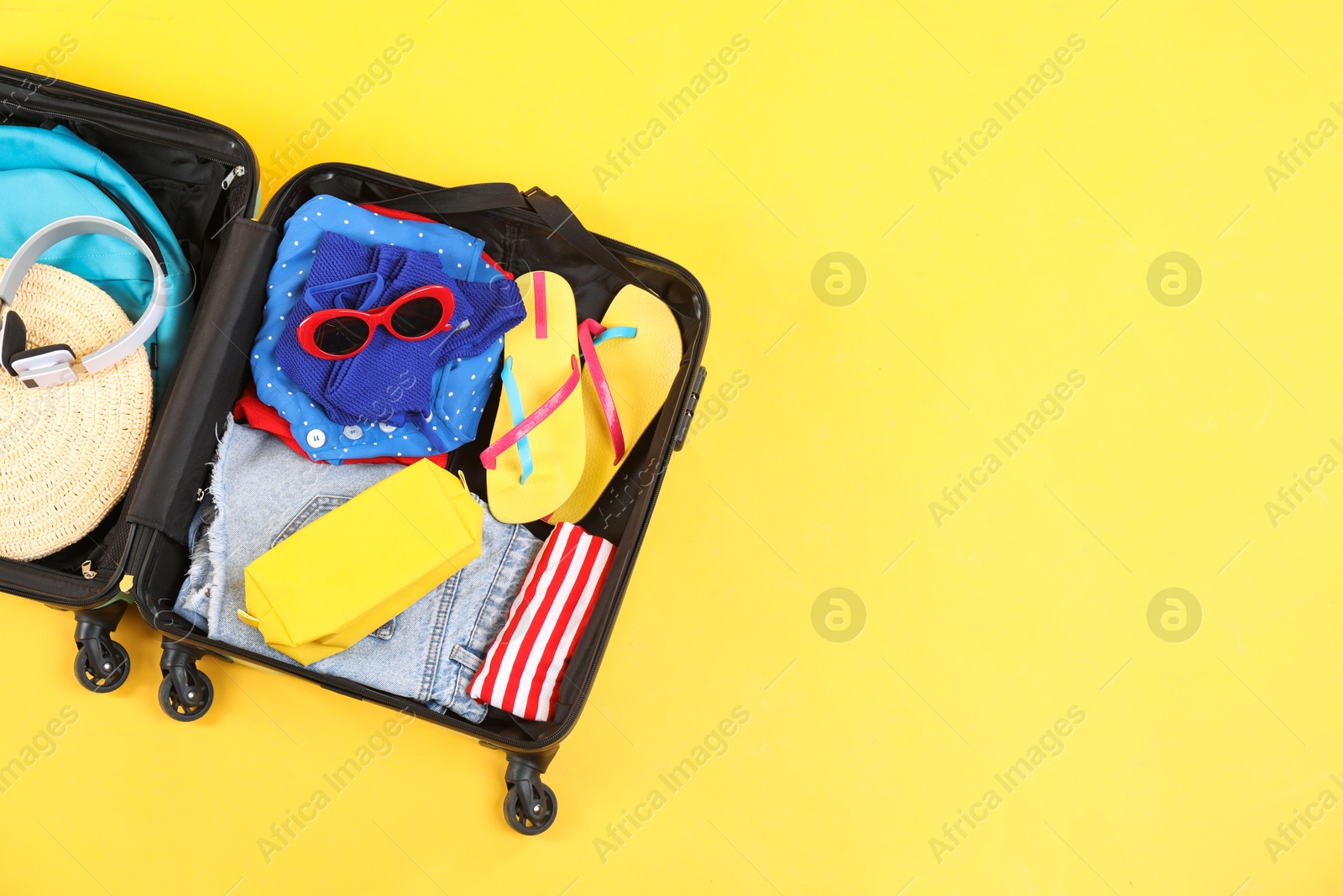 Photo of Travel abroad. Packed suitcase on yellow background, top view. Space for text