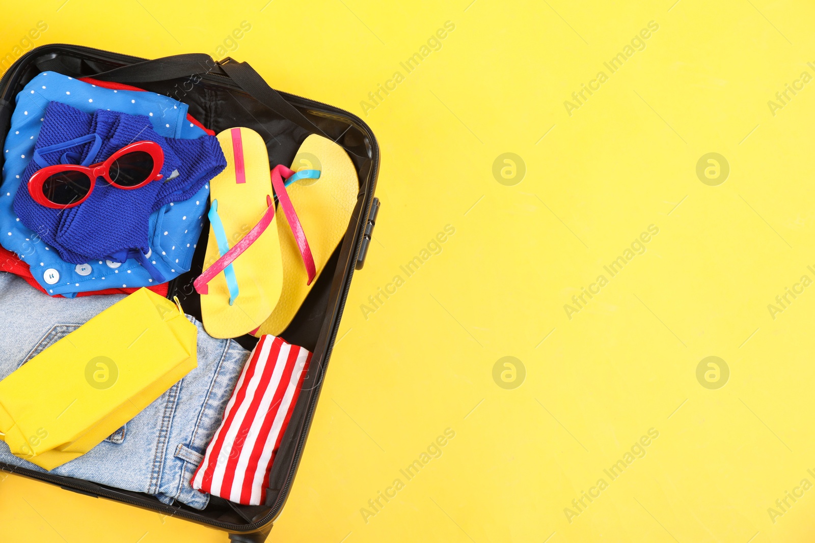 Photo of Travel abroad. Packed suitcase on yellow background, top view. Space for text