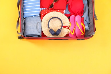 Photo of Travel abroad. Packed suitcase on yellow background, top view. Space for text