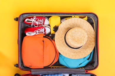 Photo of Travel abroad. Packed suitcase on yellow background, top view