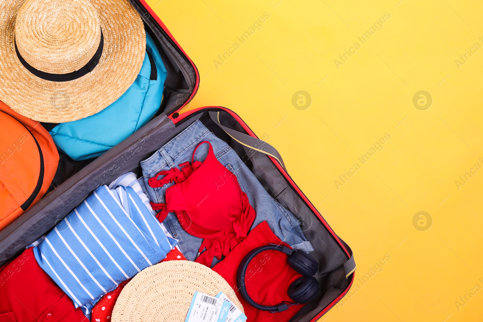 Photo of Travel abroad. Packed suitcase on yellow background, top view. Space for text